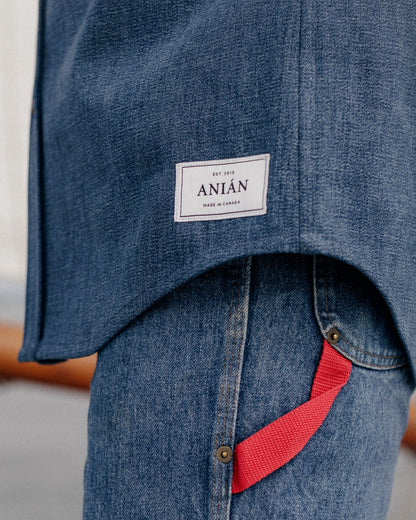 CLOSE UP PHOTO OF DARK DENIM SHIRT HEMLINE AND ANIAN TAG ON MODEL WEARING BLUE JEANS 