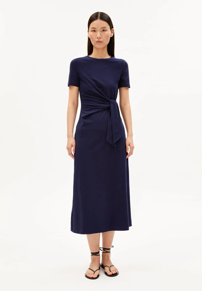 NAVY SHEATH WRAP DRESS ON MODEL WITH BLACK HAIR AND FLAT SANDALS AGAINST WHITE BACKGROUND