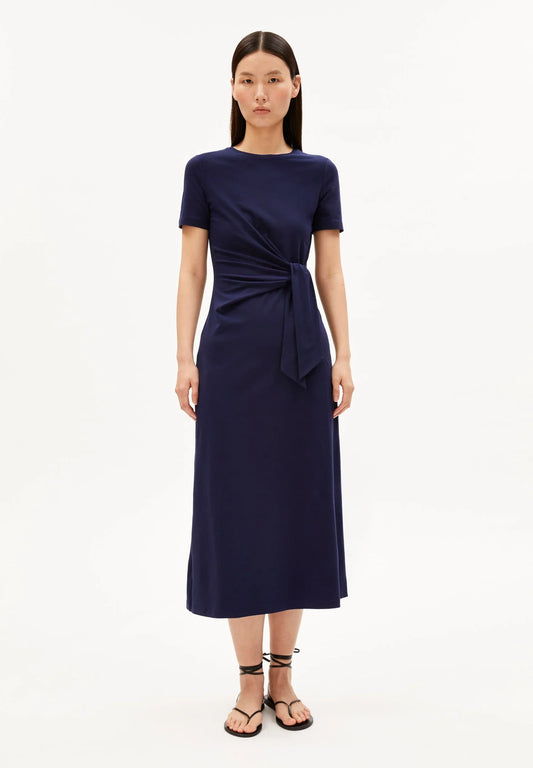 NAVY SHEATH WRAP DRESS ON MODEL WITH BLACK HAIR AND FLAT SANDALS AGAINST WHITE BACKGROUND