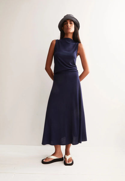 MODEL WEARING NAVY TOP AND SKIRT, GREY BUCKET HAT AND WHITE SANDALS  AGAINST A WHITE BACKGROUND