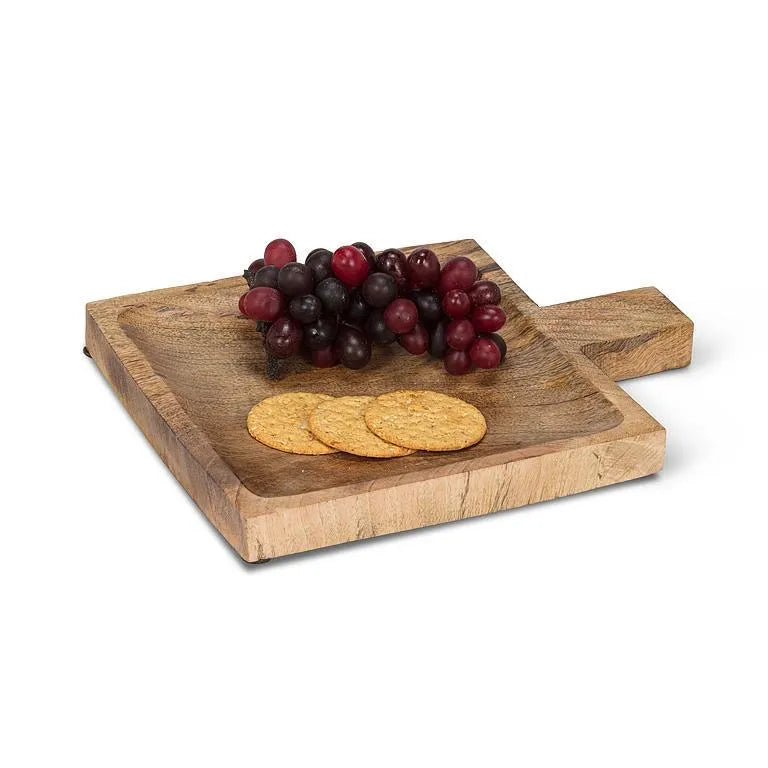 A rectangular wooden serving board with a handle, shown on a white background with grapes and crackers placed on top as props.
