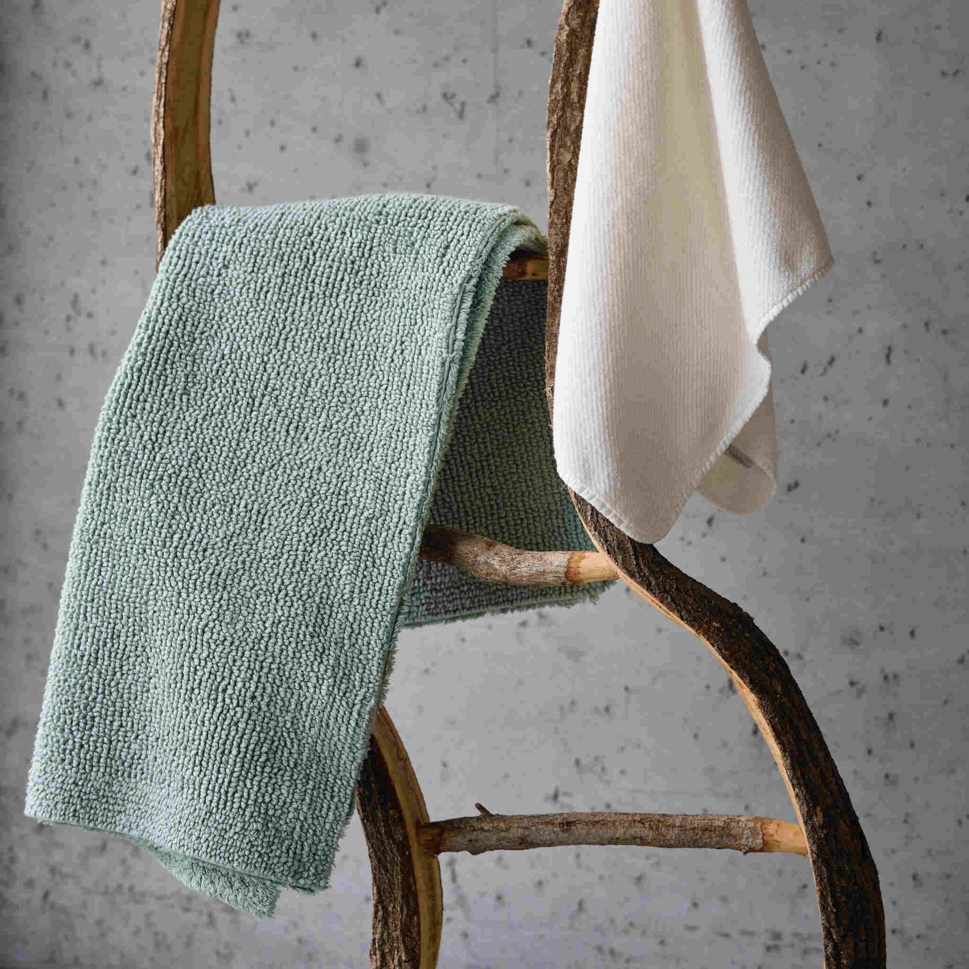 Green reversible bath mat draped over a wooden towel rack against a gray background