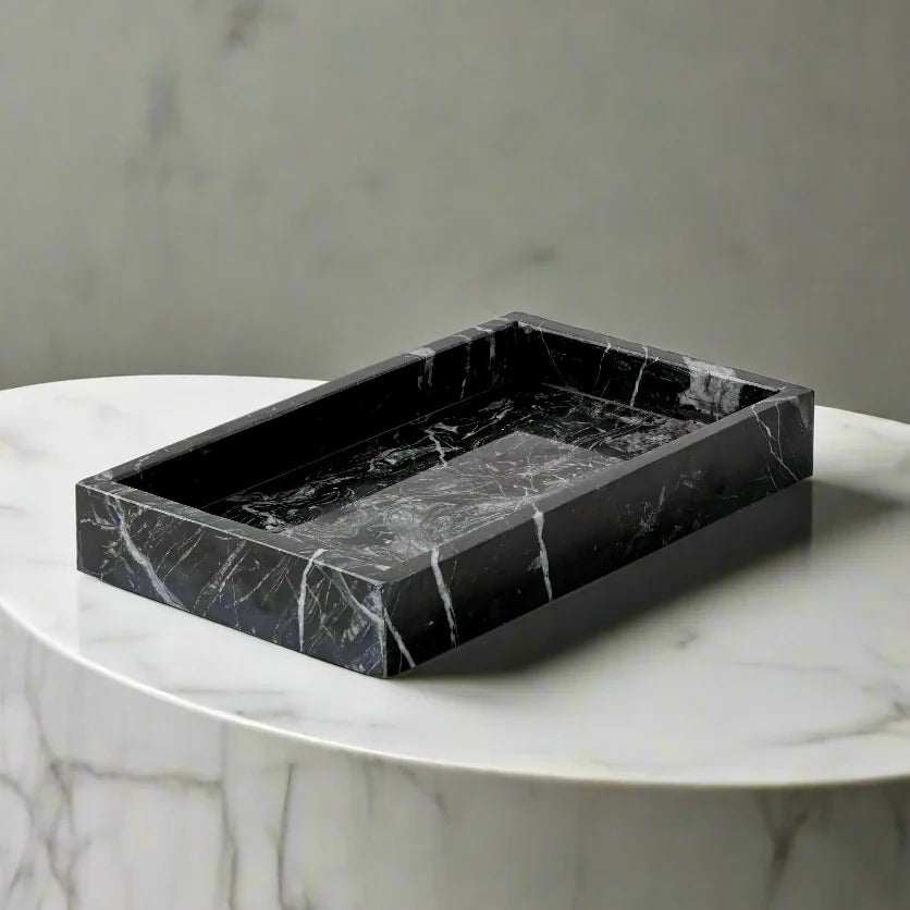 Black marble tray on a white marble pedestal against a gray background