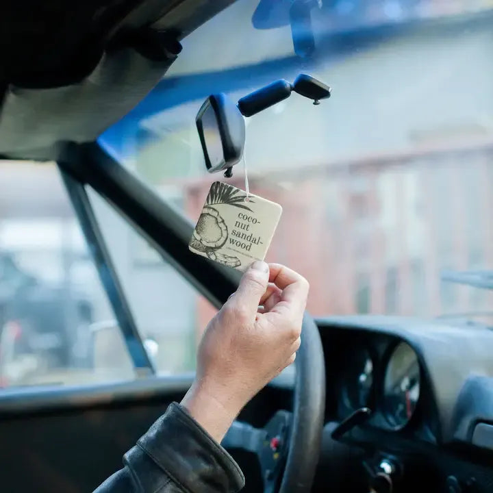 Hand holding a car air freshener tag inside a vehicle