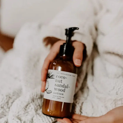 Hand holding a bottle of coconut sandalwood lotion with a soft blurred background