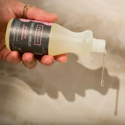 Hand holding a bottle of Eucalan Delicate Wash liquid with a visible label against a neutral background.