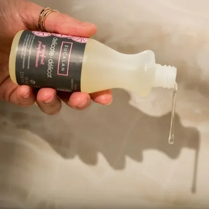 Hand holding a bottle of Eucalan Delicate Wash liquid with a visible label against a neutral background.