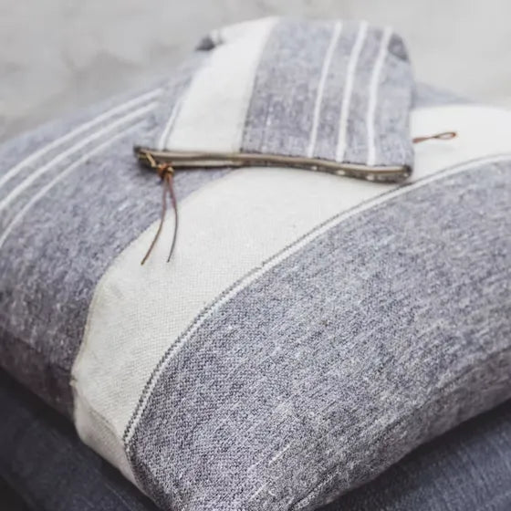 A close-up of a gray and off-white striped woven cushion with a matching folded fabric piece resting on top, photographed against a soft light gray background.