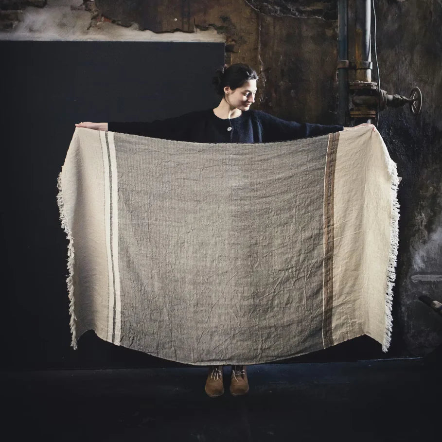 Person holding a large woven blanket with a dark background