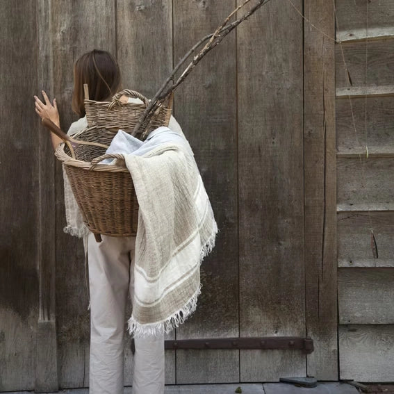Person holding a woven basket with a blanket against a wooden wall.