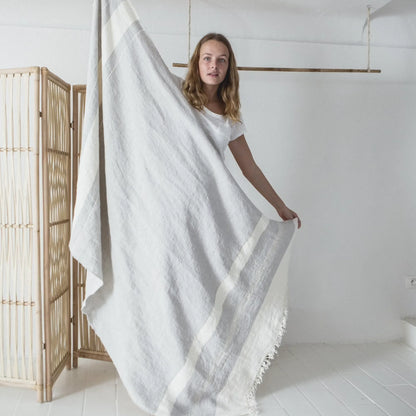 Woman holding a white textured blanket in a minimalistic room with a wooden screen.