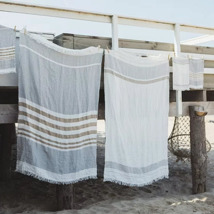 Two beach towels with striped patterns hanging on a wooden rack by the beach.