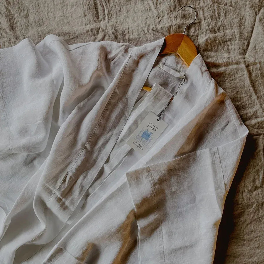 Light-colored linen bathrobe on a hanger with a textured fabric background