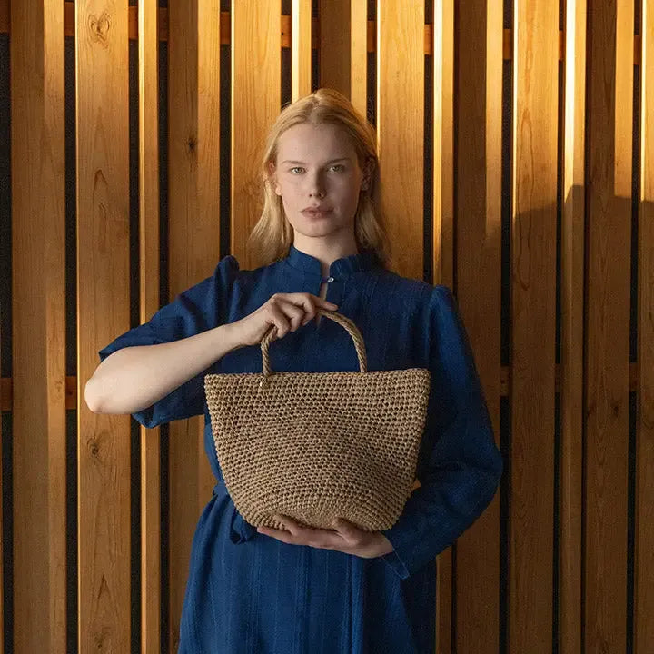 Woman holding a woven bag against a wooden paneled background