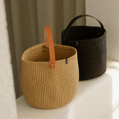 Two woven baskets with leather handles on a light surface.