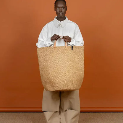 Person holding a large woven bag against an orange background