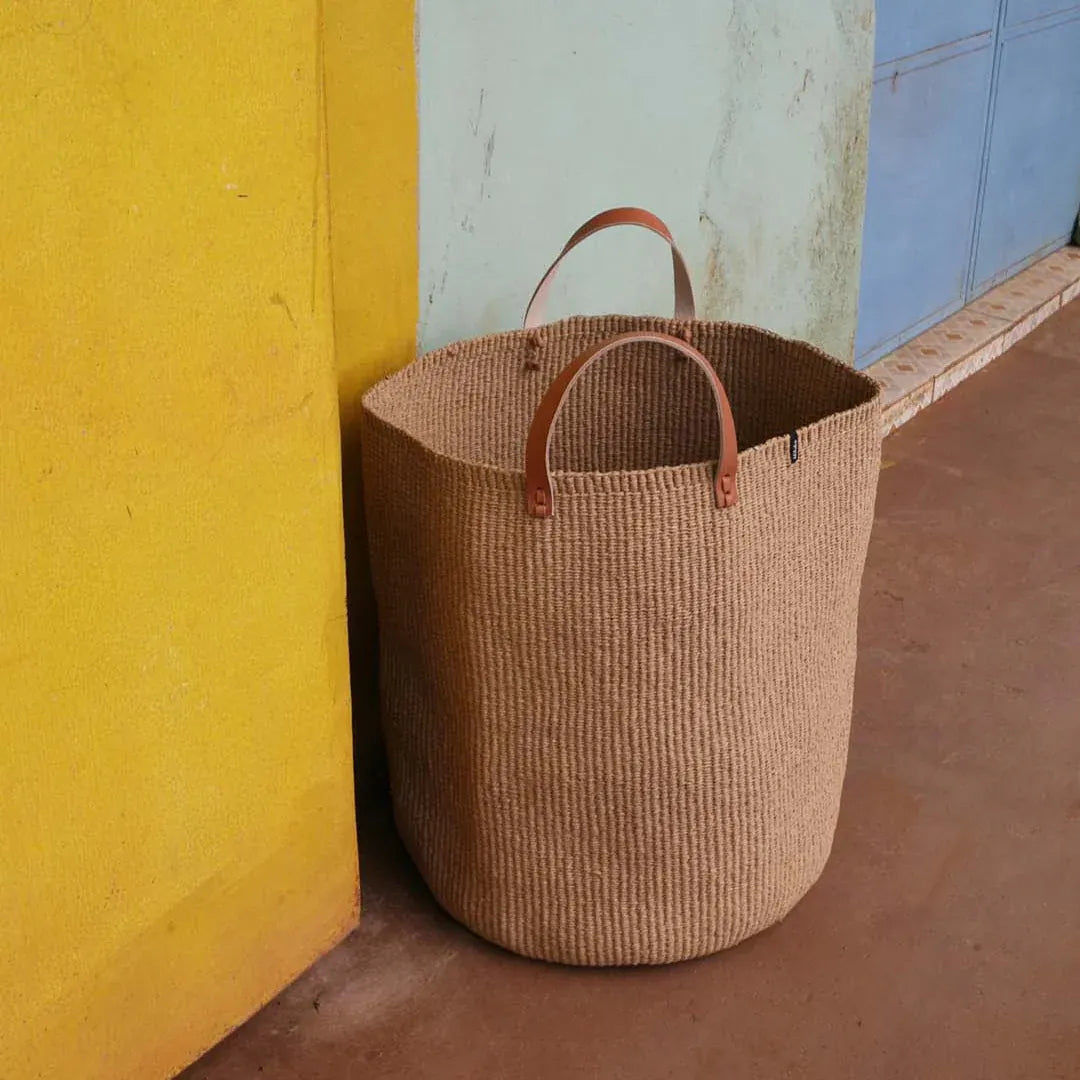 Woven basket with leather handles against a yellow wall