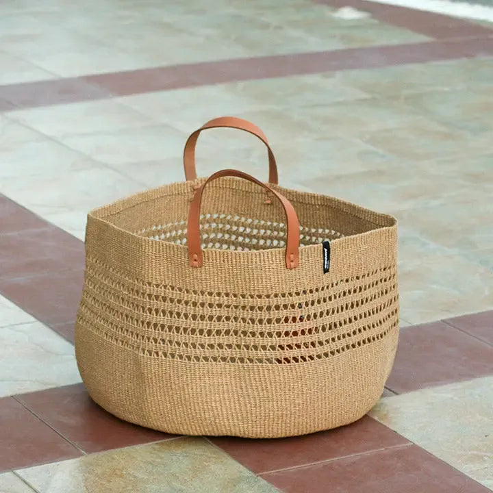Woven basket with leather handles on a tiled floor