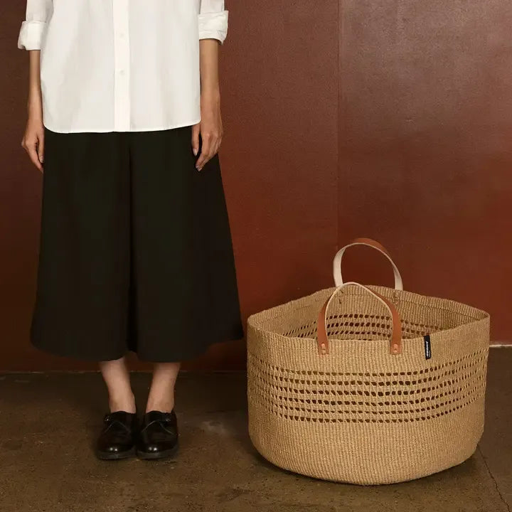 Person standing next to a woven basket against a brown wall.