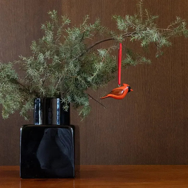 Black vase with green branches and a red cardinal ornament on a wooden surface.