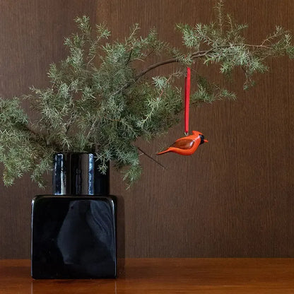 Black vase with green branches and a red cardinal ornament on a wooden surface.