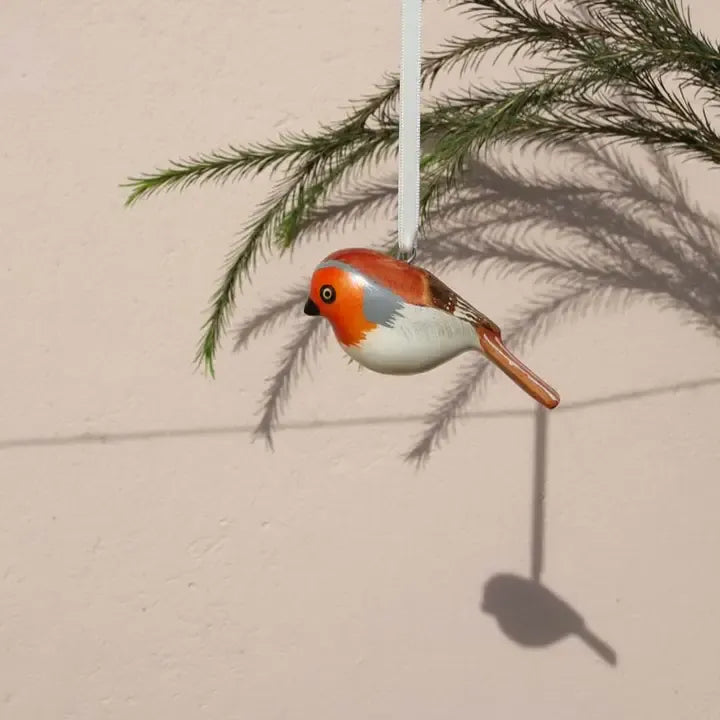Decorative bird ornament hanging from a branch against a beige wall.
