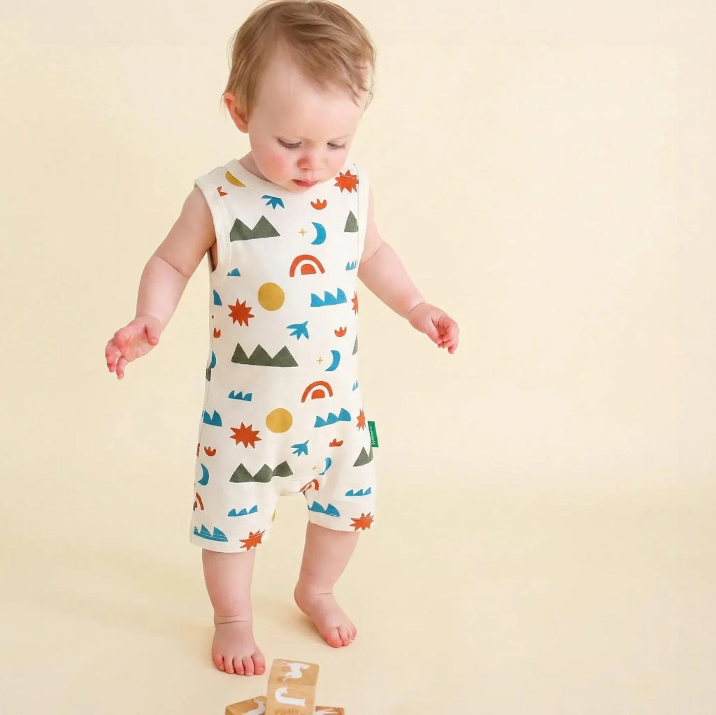 Baby wearing a colorful patterned romper on a beige background