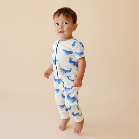 Child wearing a white onesie with blue whale patterns on a beige background