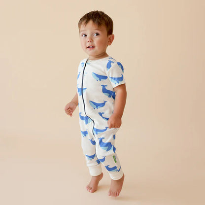 Child wearing a white onesie with blue whale patterns on a beige background