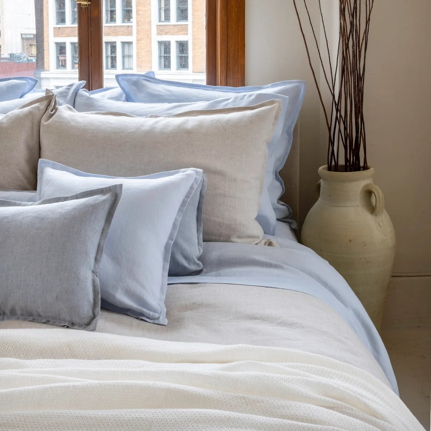 Neatly arranged pillows on a bed with a vase in the background