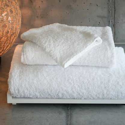 Stack of white textured towels on a wooden surface with a concrete wall background