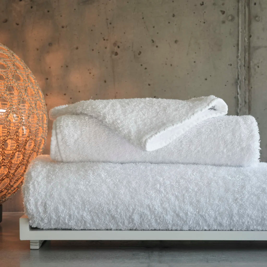 Stack of white textured towels on a wooden surface with a decorative lamp in the background.