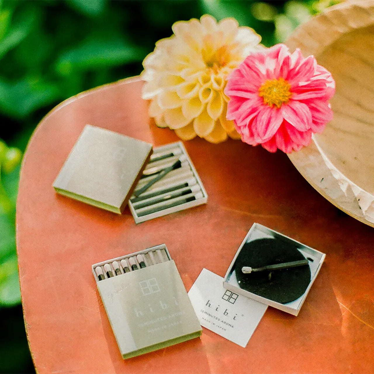 Matches and matches holder on a wooden surface with flowers in the background