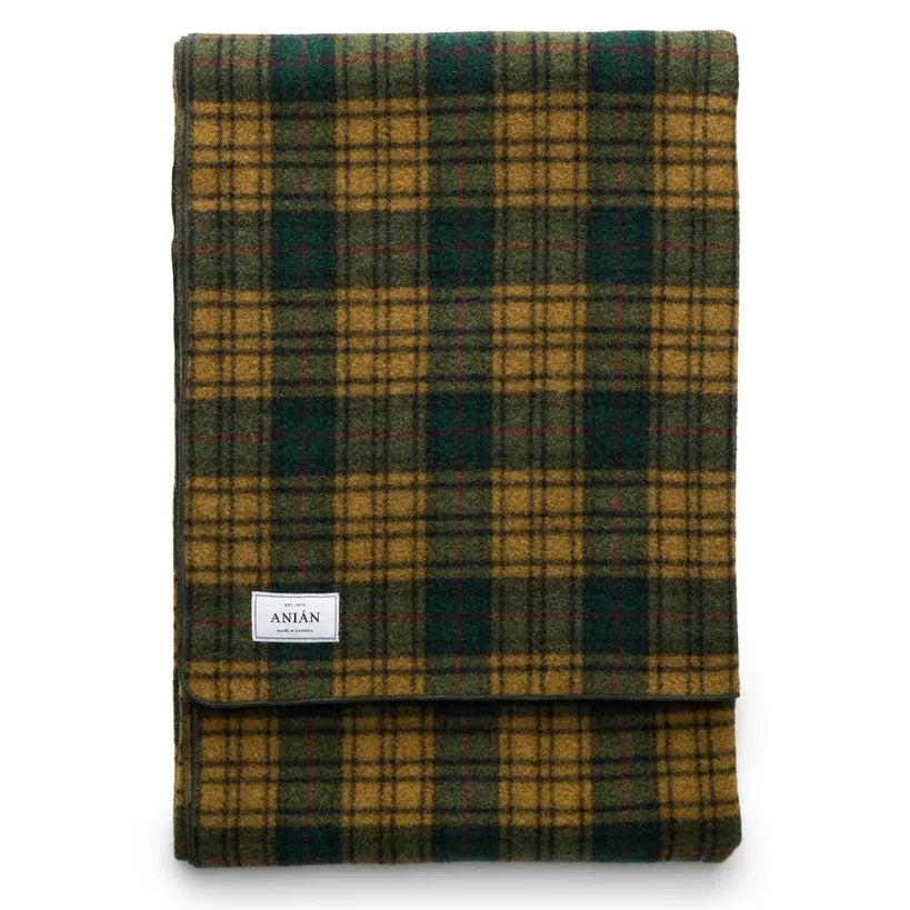 A folded plaid blanket in a mustard yellow and dark green tartan pattern, featuring a small white brand label that reads 'ANiÁN'.