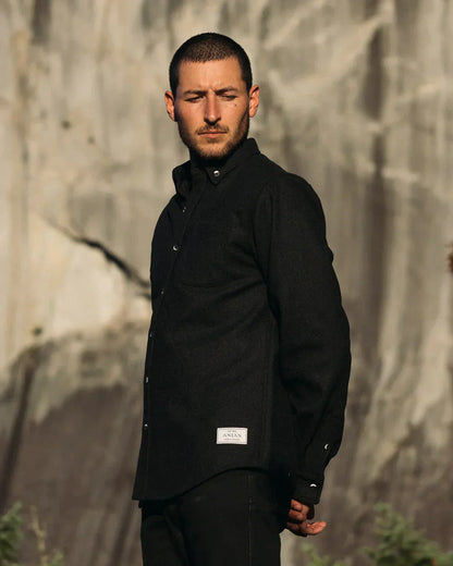 Man wearing a black jacket standing against a textured wall.