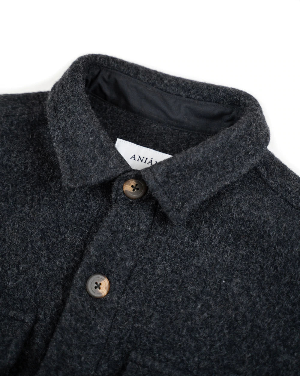Close-up of a dark charcoal gray textured wool coat with a pointed collar, brown buttons, and a white brand label reading 'ANIAN' on a white background.