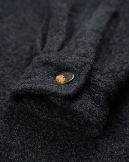 Close-up of a dark charcoal gray textured knit garment, showing a folded cuff with a small round brown button.