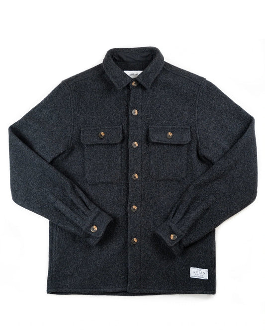 A dark charcoal gray wool button-up shirt jacket with brown buttons, laid flat on a white background. It features a classic collar, two buttoned chest pockets, and a small white woven label near the bottom right hem.