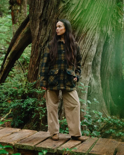 Person standing on a wooden platform in a forest with a large tree behind them wearing a plaid wool coat