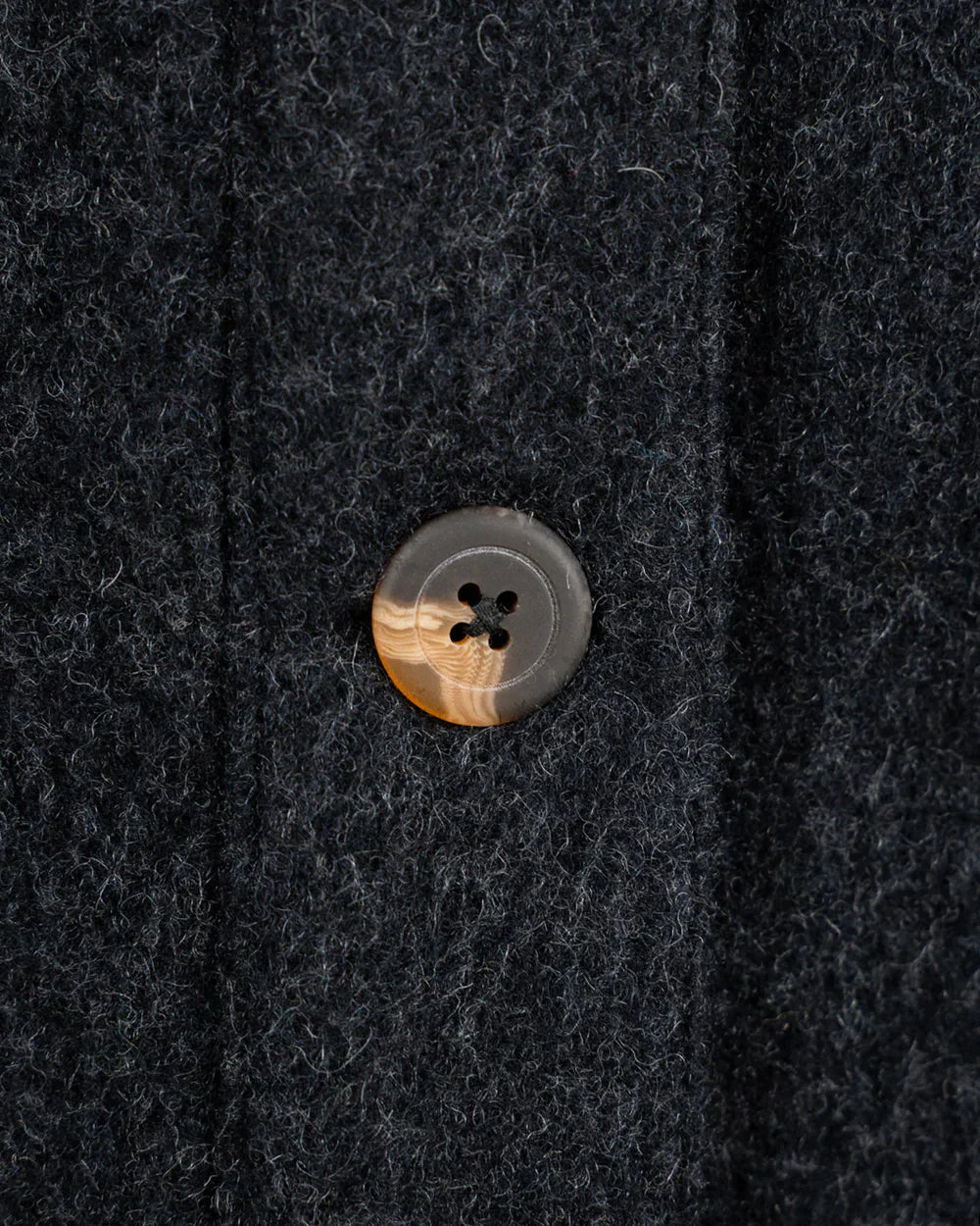 Close-up of a dark charcoal wool fabric with a single round button featuring a tiger-striped pattern in brown, beige, and gray.