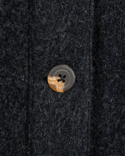 Close-up of a dark charcoal wool fabric with a single round button featuring a tiger-striped pattern in brown, beige, and gray.