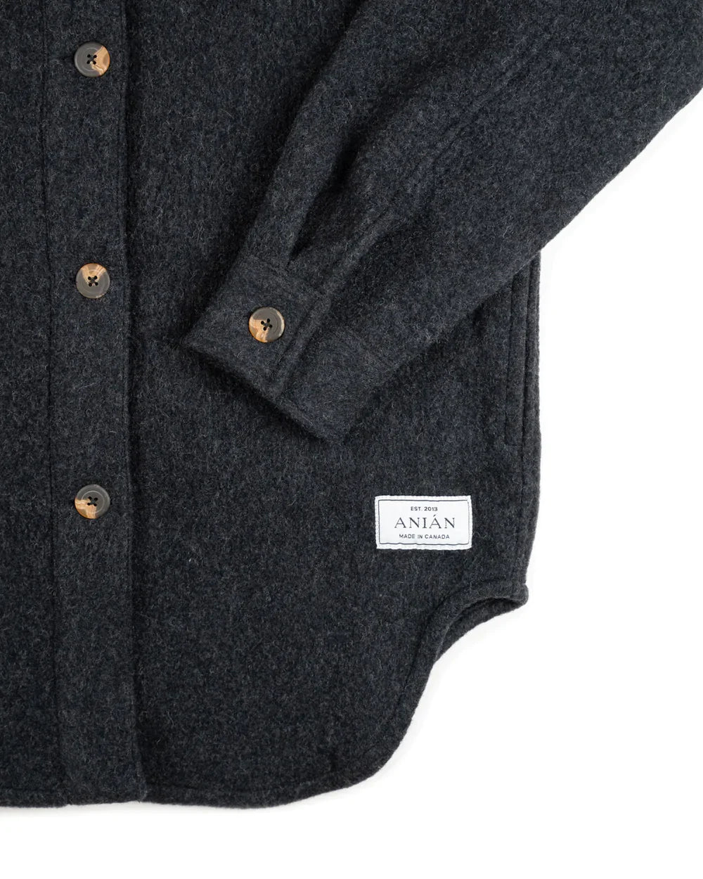 Close-up of a dark charcoal gray wool button-up shirt jacket with brown buttons and a white brand label reading 'The Men of ANIAN'.