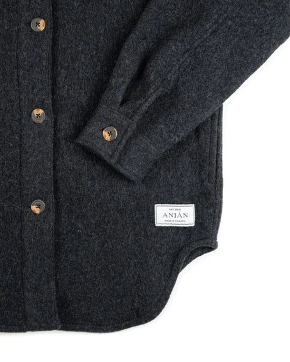 Close-up of a dark charcoal gray wool button-up shirt jacket with brown buttons and a white brand label reading 'The Men of ANIAN'.
