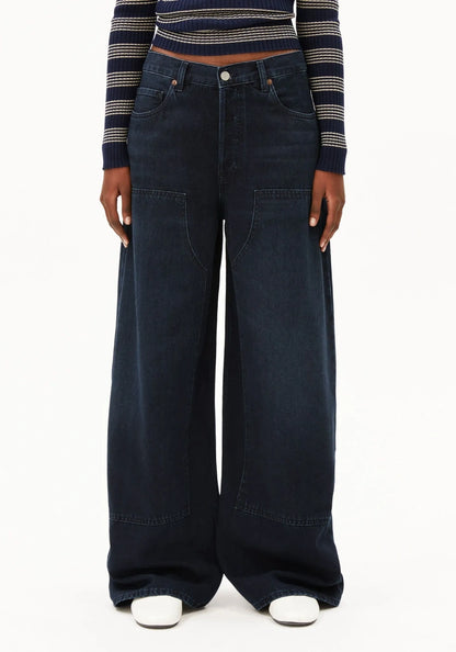 A model wearing dark wash wide-leg denim jeans with a striped long-sleeve crop top and white sneakers, shown from the waist down against a plain white background.