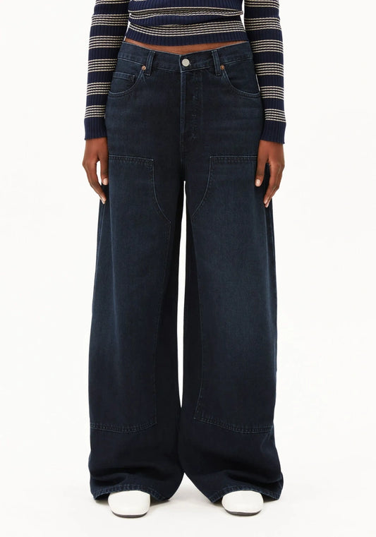 A model wearing dark wash wide-leg denim jeans with a striped long-sleeve crop top and white sneakers, shown from the waist down against a plain white background.