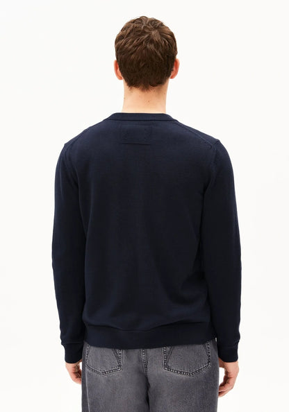 A man viewed from behind wearing a dark navy long-sleeve crewneck sweater and gray jeans against a plain white background.