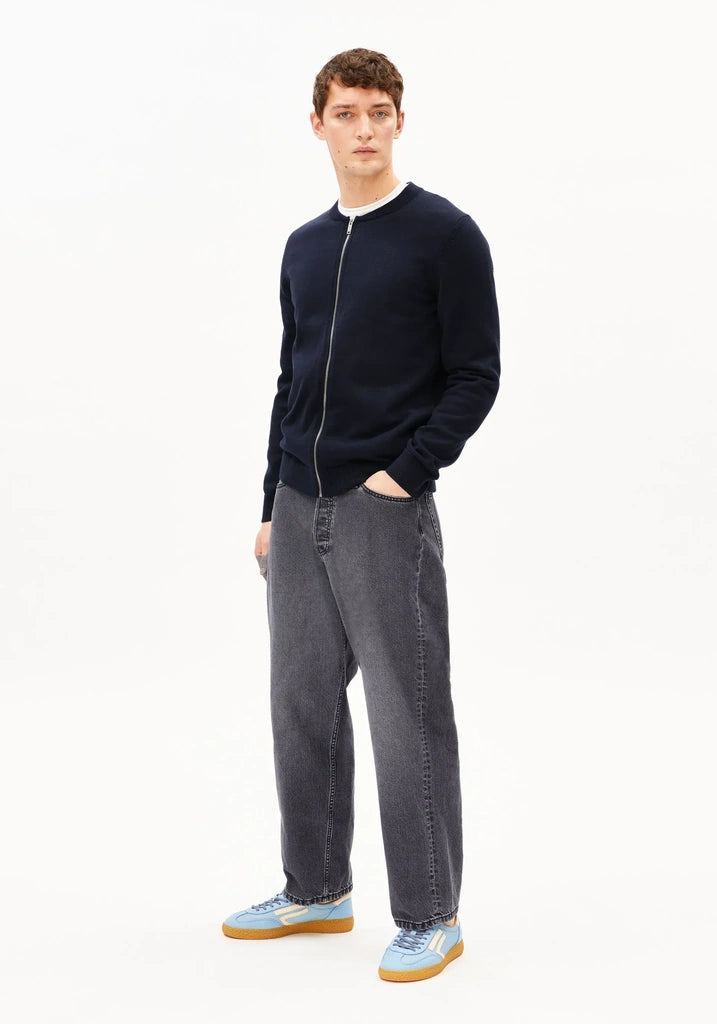Man wearing a navy sweater and gray jeans on a white background