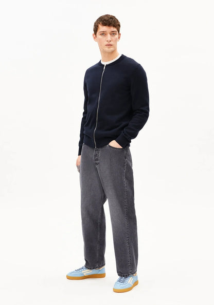 Man wearing a navy sweater and gray jeans on a white background