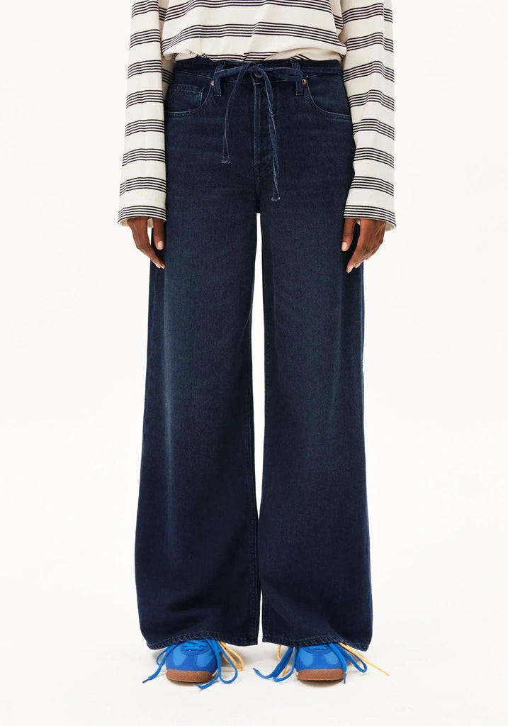 A person wearing dark blue wide-leg drawstring jeans, a cream and navy striped long-sleeve top, and blue lace-up shoes against a plain white background.