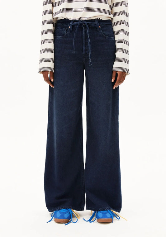 A person wearing dark blue wide-leg drawstring jeans, a cream and navy striped long-sleeve top, and blue lace-up shoes against a plain white background.